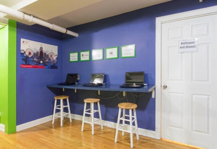 Wrigley Hostel's adult-only, gay-friendly hotel room. Laptops on a desk with stools. A bathroom door is visible. Budget travel.