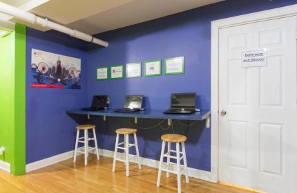 Wrigley Hostel's adult-only, gay-friendly hotel room. Laptops on a desk with stools. A bathroom door is visible. Budget travel.