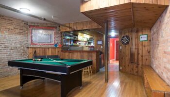 Wrigley Hostel Adults Only game room. Pool table, dartboard, and bar area in a gay-friendly hotel. Wood paneling and exposed brick details.