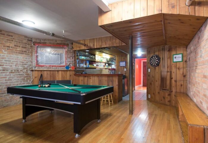 Wrigley Hostel Adults Only game room. Pool table, dartboard, and bar area in a gay-friendly hotel. Wood paneling and exposed brick details.