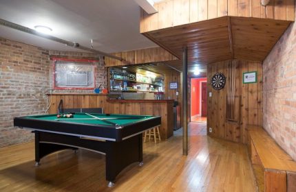 Wrigley Hostel Adults Only game room. Pool table, dartboard, and bar area in a gay-friendly hotel. Wood paneling and exposed brick details.