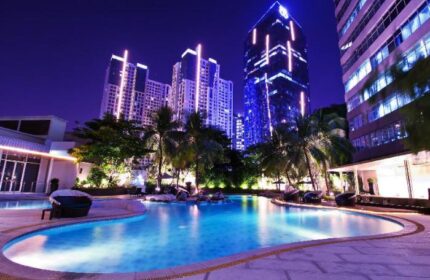 Night view of Wyndham Casablanca Jakarta's pool, a gay-friendly hotel. Skyscrapers and palm trees surround the illuminated pool area.