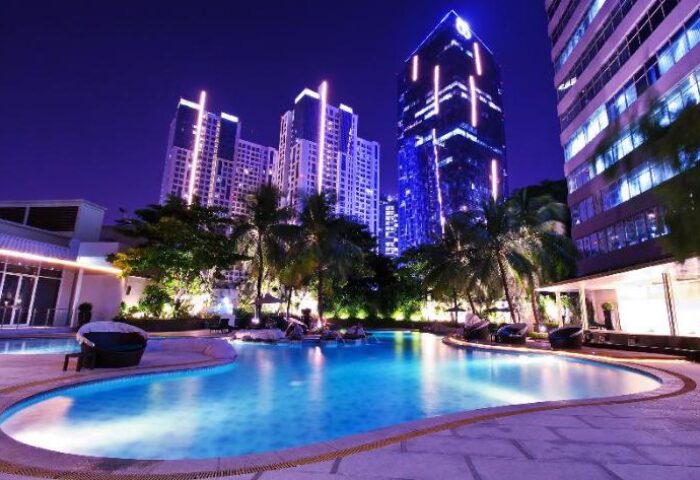Night view of Wyndham Casablanca Jakarta's pool, a gay-friendly hotel. Skyscrapers and palm trees surround the illuminated pool area.