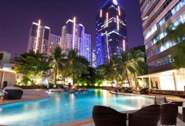 Wyndham Casablanca Jakarta gay-friendly hotel pool at night. Modern buildings, palm trees, and lounge chairs create a relaxing atmosphere.