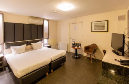 XO Hotels City Centre gay-friendly hotel room. Two beds with white linens, dark headboard. Desk, chair, TV, coffee maker. Modern decor.