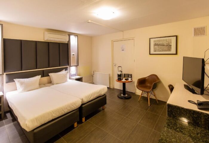XO Hotels City Centre gay-friendly hotel room. Two beds with white linens, dark headboard. Desk, chair, TV, coffee maker. Modern decor.