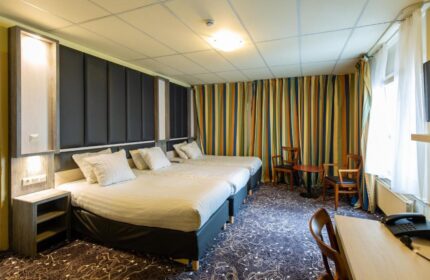 XO Hotels City Centre room with two beds, desk, chairs, and striped curtains. Gay-friendly hotel room for travelers.
