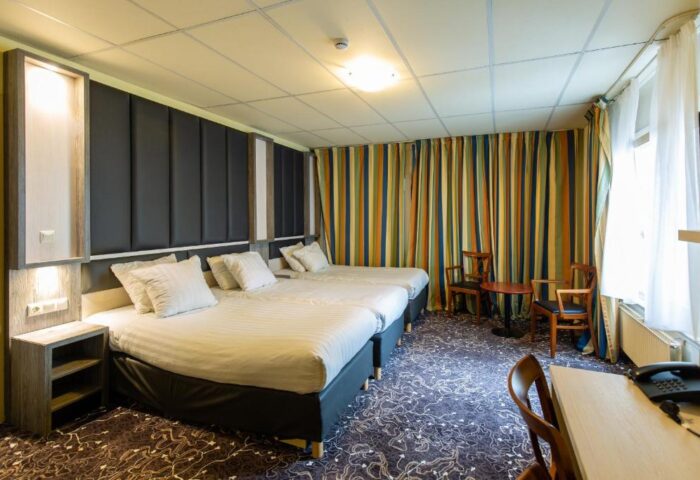 XO Hotels City Centre room with two beds, desk, chairs, and striped curtains. Gay-friendly hotel room for travelers.