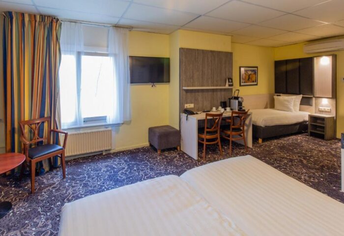 XO Hotels City Centre gay-friendly room. Twin beds, desk, chairs, TV, and window with curtains. Comfortable stay in Amsterdam.