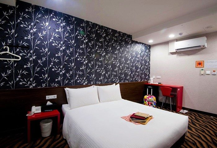 Ximen Holiday Fun Hotel room. Gay-friendly hotel with a double bed, floral wallpaper, red accents, and a suitcase. Comfy stay in Taiwan.