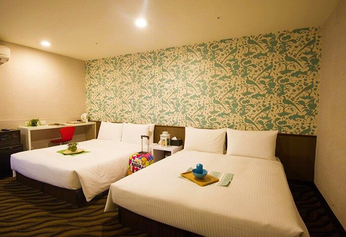 Ximen Holiday Fun Hotel room. Gay-friendly hotel in Ximen, Taipei. Two beds, patterned wallpaper, desk, & colorful suitcase. Great for gay travel.