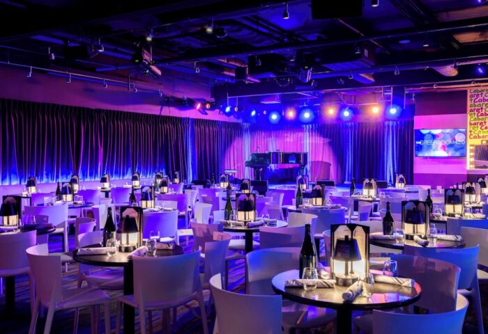 YOTEL New York Times Square's Green Room 42, a gay-friendly hotel venue. Tables set for cabaret show, stage with piano, purple lighting.