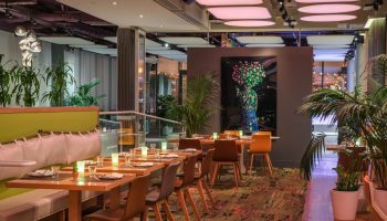 YOTEL New York Times Square interior. Gay-friendly hotel restaurant with tables, chairs, plants, and modern decor. Upscale dining.