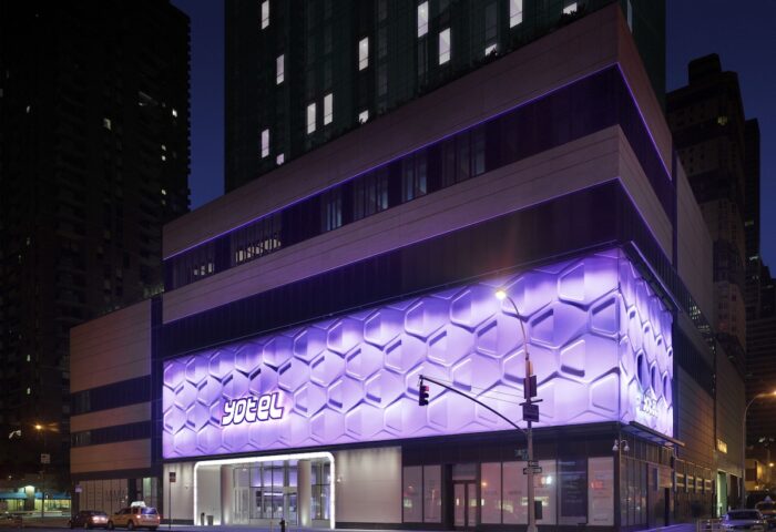 YOTEL Times Square, a gay-friendly hotel in New York. Exterior view at night with purple honeycomb lighting. Great for gay travelers' stay.