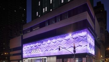 YOTEL Times Square, a gay-friendly hotel in New York. Exterior view at night with purple honeycomb lighting. Great for gay travelers' stay.