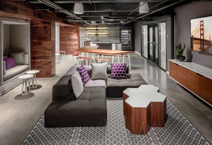 YOTEL San Francisco's stylish lounge. A gay-friendly hotel with modern design, featuring a modular sofa, communal table, and Golden Gate Bridge TV art.