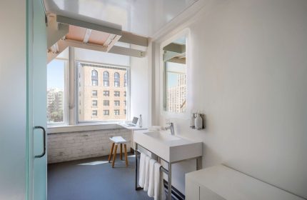 YOTEL San Francisco bathroom view. Modern design, white fixtures, window view, and a laptop. Gay-friendly hotel for travelers.