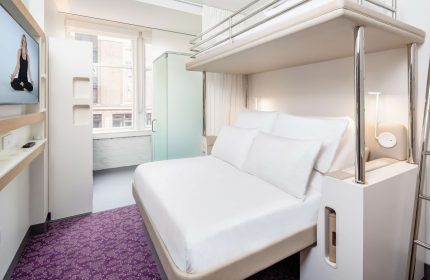 YOTEL San Francisco room. Modern hotel room with bunk bed, white linens, purple carpet, and TV. Gay-friendly hotel for gay men traveling.
