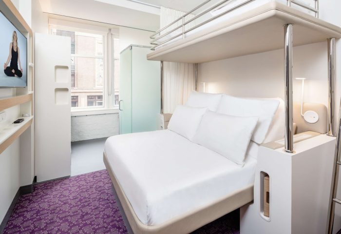 YOTEL San Francisco room. Modern hotel room with bunk bed, white linens, purple carpet, and TV. Gay-friendly hotel for gay men traveling.