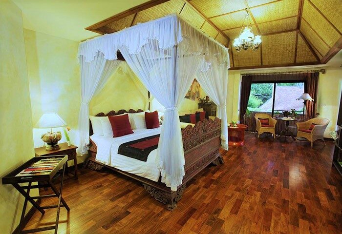 Yaang Come Village Hotel's gay-friendly room. Canopy bed with red accents, balcony seating. Upscale lodging for gay travelers.