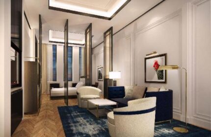 Yangon Excelsior gay-friendly hotel room. Living area with blue rug, sofa, chairs, and art. Bedroom with bed visible through room dividers.
