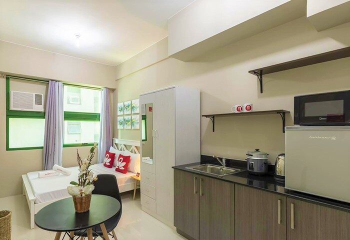 ZEN Rooms Symphony Timog Ave QC gay-friendly hotel room. Interior view with bed, kitchenette, table, and chair. Modern, clean design.