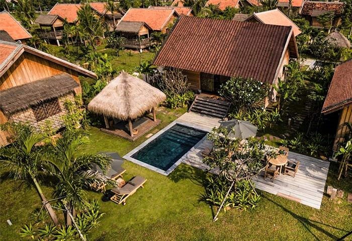 Aerial view of Zannier Hotels Phum Baitang, a gay-friendly hotel. Features villas, a pool, thatched roofs, and lush greenery. Perfect for gay travel.