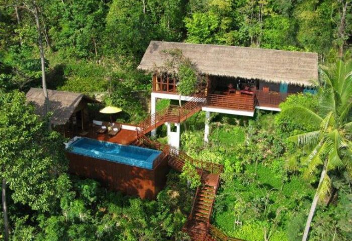 Zeavola Hotel: Gay-friendly hotel aerial view. Lush greenery surrounds villas with pools and thatched roofs. Tropical gay travel.