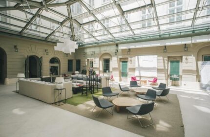Zenit Budapest Palace's interior. A gay-friendly hotel with a glass ceiling, seating areas, and modern design. A welcoming space for gay travelers.