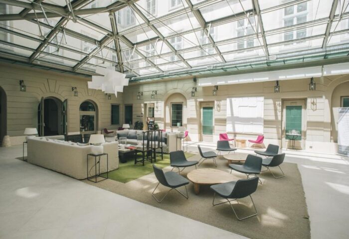 Zenit Budapest Palace's interior. A gay-friendly hotel with a glass ceiling, seating areas, and modern design. A welcoming space for gay travelers.