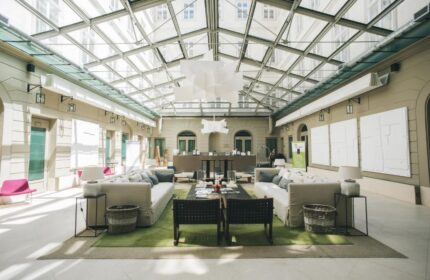 Zenit Budapest Palace's stylish lobby with a glass roof. Gay-friendly hotel with modern decor, sofas, and a welcoming atmosphere for gay travelers.