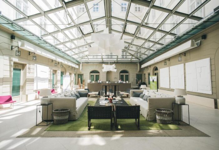Zenit Budapest Palace's stylish lobby with a glass roof. Gay-friendly hotel with modern decor, sofas, and a welcoming atmosphere for gay travelers.