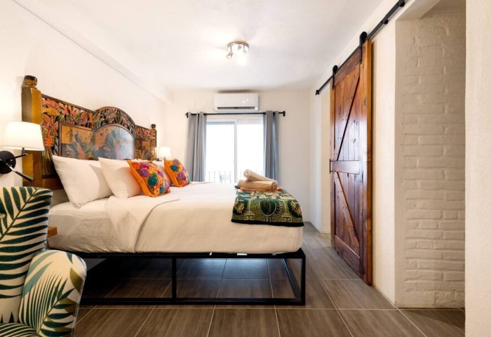 ZonaZ Boutique Hotel bedroom. Gay-friendly hotel room with a king-size bed, colorful pillows, and a rustic wood sliding door. Modern, stylish decor.