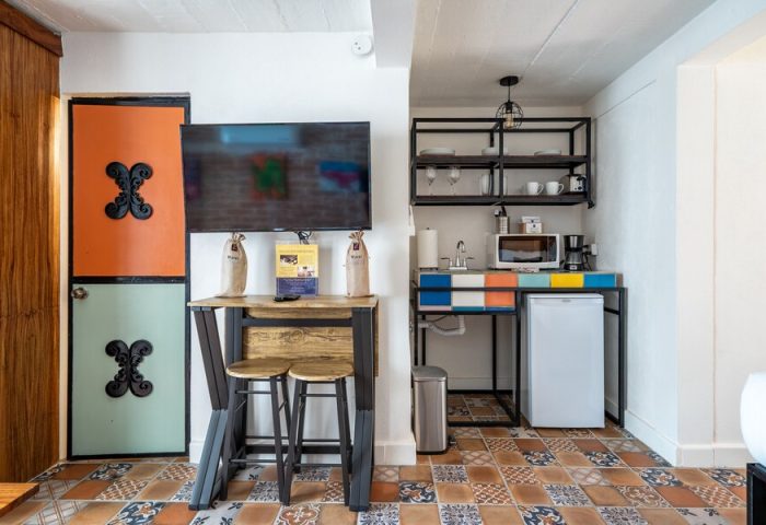 ZonaZ Boutique Hotel gay-friendly room. Kitchenette with microwave, fridge, sink, and shelving. Table with stools. Colorful tile floor.