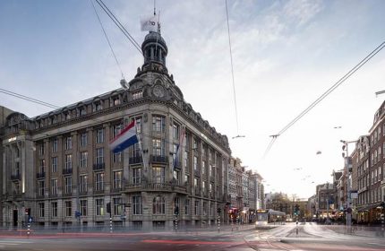 art'otel Amsterdam, a gay-friendly hotel. Exterior view of the hotel with Dutch flags and city street. Amsterdam travel advice.