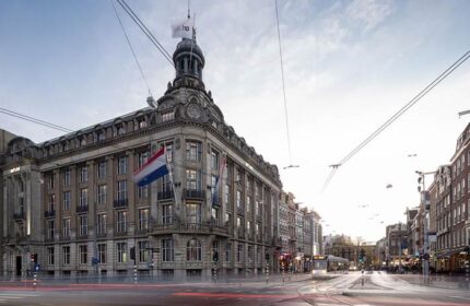 art'otel Amsterdam, a gay-friendly hotel. Exterior view of the hotel with Dutch flags and city street. Amsterdam travel advice.