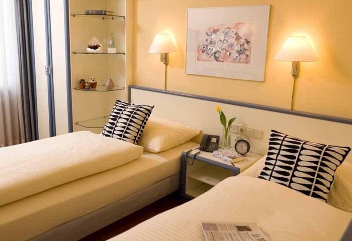 carathotel Munchen City twin room. Gay-friendly hotel with two beds, bedside table, lamps, and modern decor. Ideal for gay travelers in Munich.