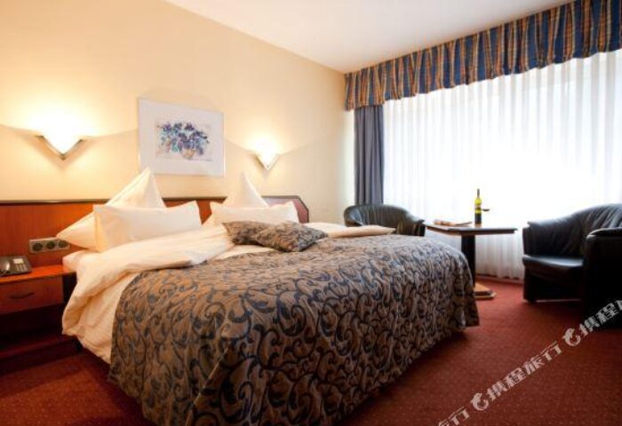 Carathotel Munchen City room. Gay-friendly hotel bedroom with a double bed, chairs, and a table with a bottle of wine. Munich travel.