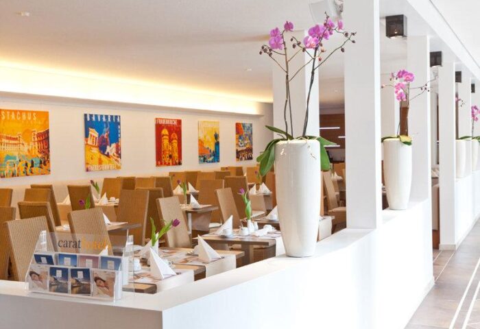 Dining area at gay-friendly carathotel Munchen City. Tables set, orchid decor, and colorful Munich landmark posters. A welcoming space.