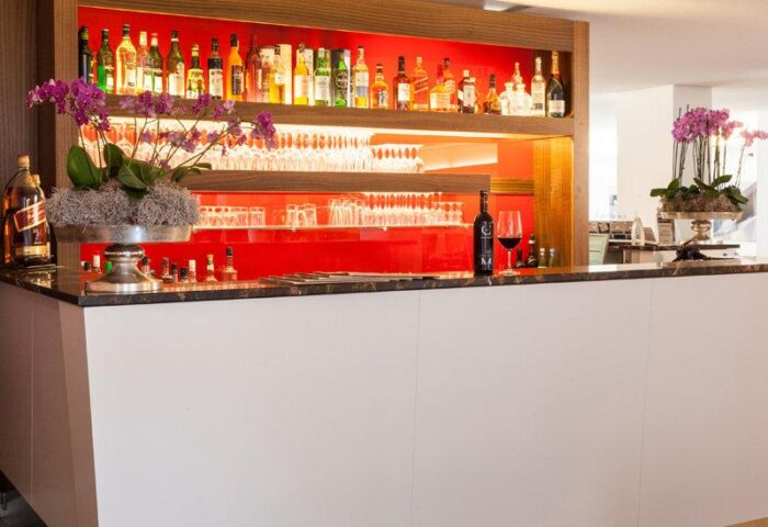 Bar area at carathotel Munchen City, a gay-friendly hotel. Liquor bottles, glassware, and orchids adorn the counter. Perfect for gay travel.