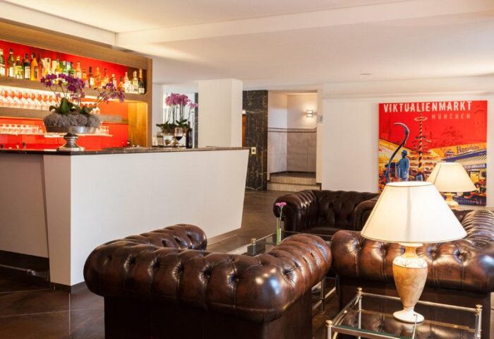 Carathotel Munchen City's bar area: Brown leather couches, glass tables, and a well-stocked bar. Gay-friendly hotel in Munich, Germany.