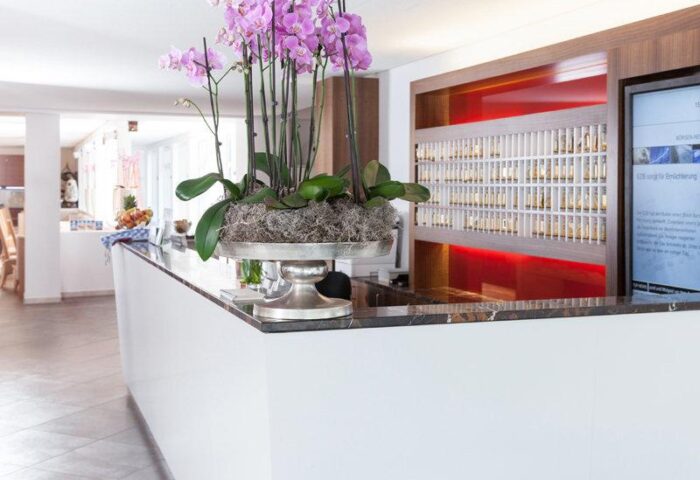Carathotel Munchen City's reception area. This gay-friendly hotel features a sleek white counter with orchid centerpiece. Modern, welcoming design.