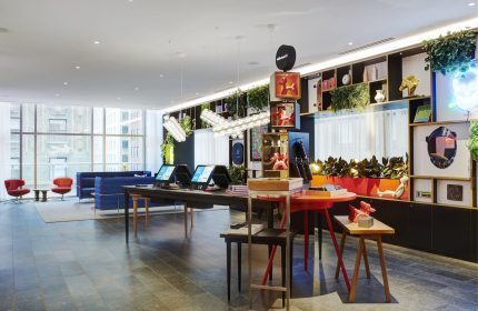 citizenM Chicago Downtown lobby, a gay-friendly hotel. Modern design with colorful decor, plants, and city views. Check-in kiosks visible.