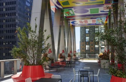 citizenM Chicago Downtown gay-friendly hotel outdoor terrace. Tables, chairs, and benches with colorful ceiling art. Urban setting.