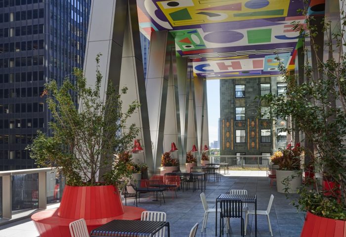 citizenM Chicago Downtown gay-friendly hotel outdoor terrace. Tables, chairs, and benches with colorful ceiling art. Urban setting.