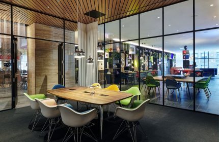 citizenM Chicago Downtown's gay-friendly hotel interior. Modern meeting space with colorful chairs around a wooden table, glass walls, and stylish decor.