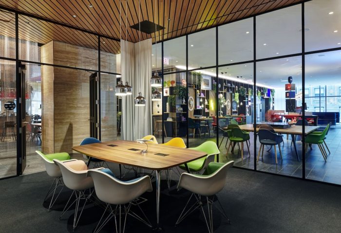 citizenM Chicago Downtown's gay-friendly hotel interior. Modern meeting space with colorful chairs around a wooden table, glass walls, and stylish decor.