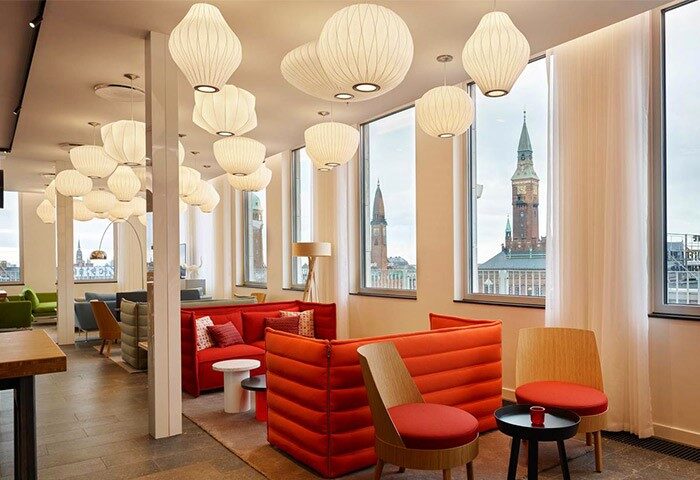 citizenM Copenhagen Radhuspladsen hotel interior. Gay-friendly hotel lounge area with stylish lighting, red seating, and city views.