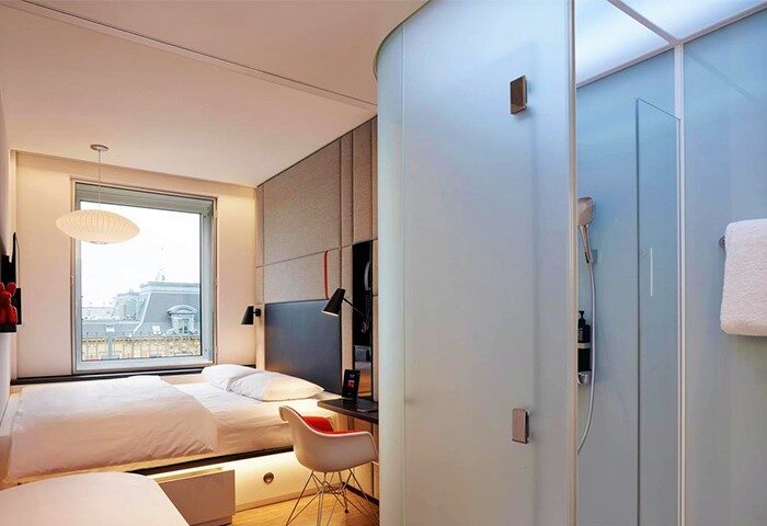citizenM Copenhagen Radhuspladsen hotel room interior. Modern design, bed, desk, and frosted glass shower. Gay-friendly hotel for travelers.