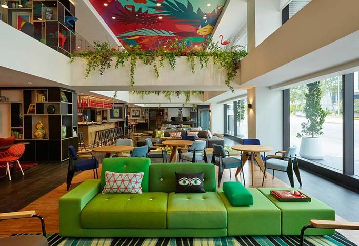 citizenM Kuala Lumpur Bukit Bintang lobby. Gay-friendly hotel seating area with green sofa, tables, and colorful ceiling art.